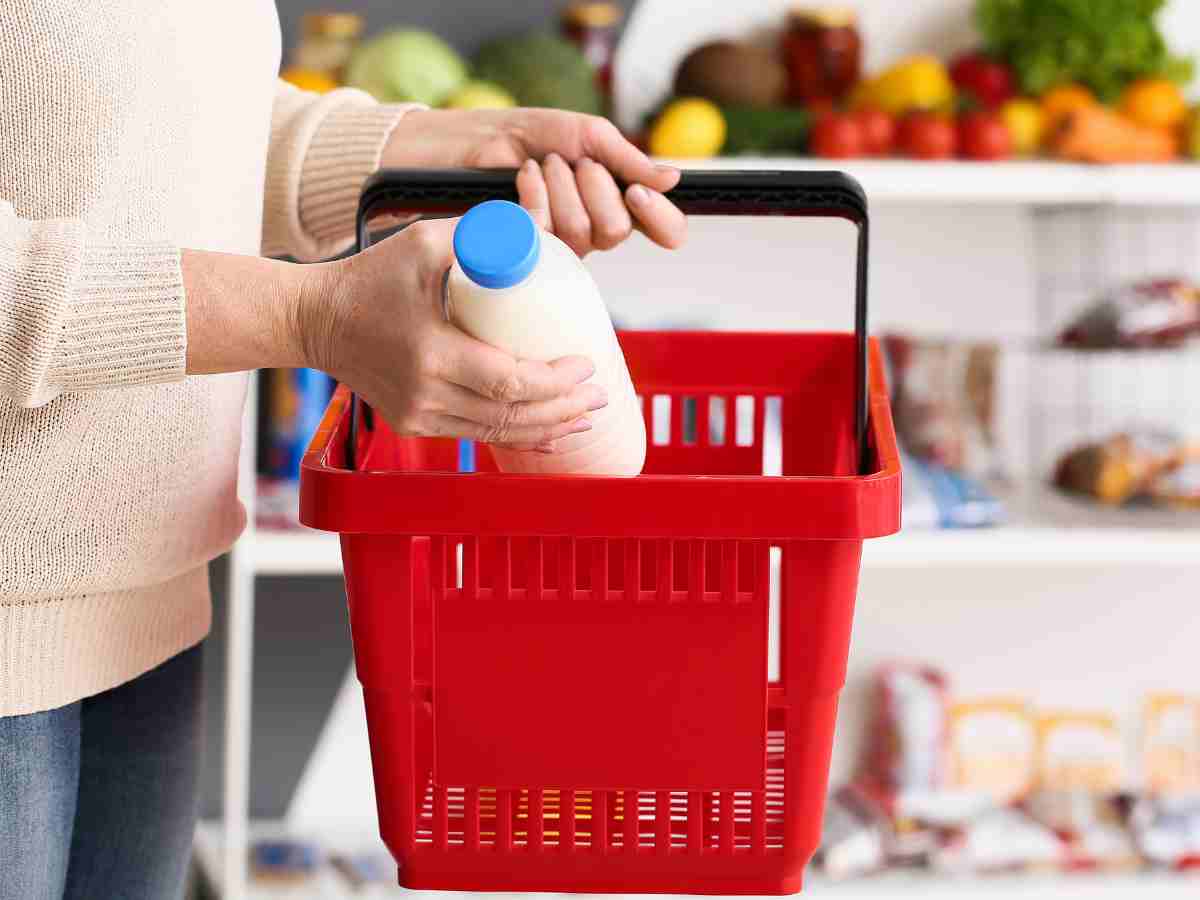 una mano mette il latte in un cestino della spesa