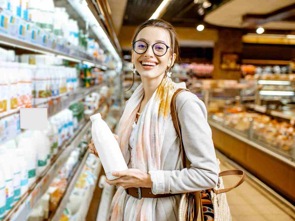 donna sorridente tra gli scaffali del supermercato con una bottiglia di latte in mano