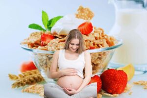 sullo sfondo tazza di cereali con fragole e yogurt in primo piano donna in gravidanza