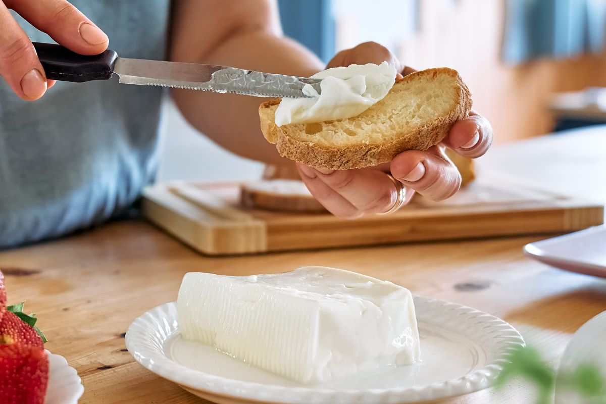 donna che spalma lo stracchino su una fetta di pane, stracchino in un piatto in primo piano